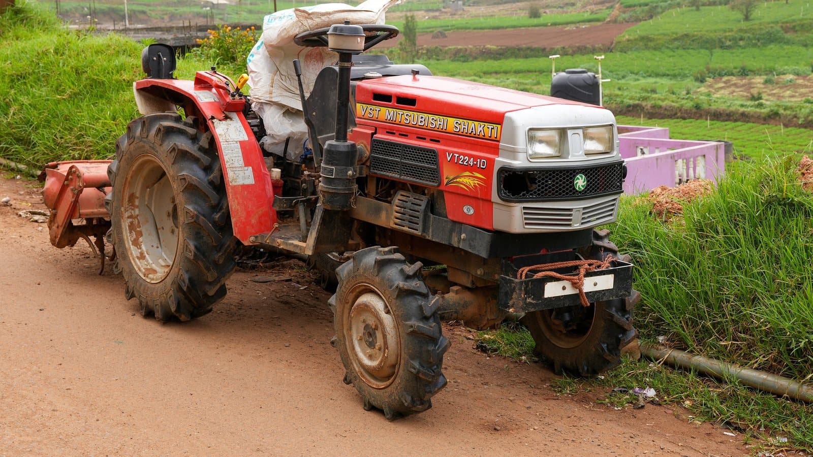 A compact tractor with a rear-mounted rotavator parked beside terraced fields in the Nilgiris