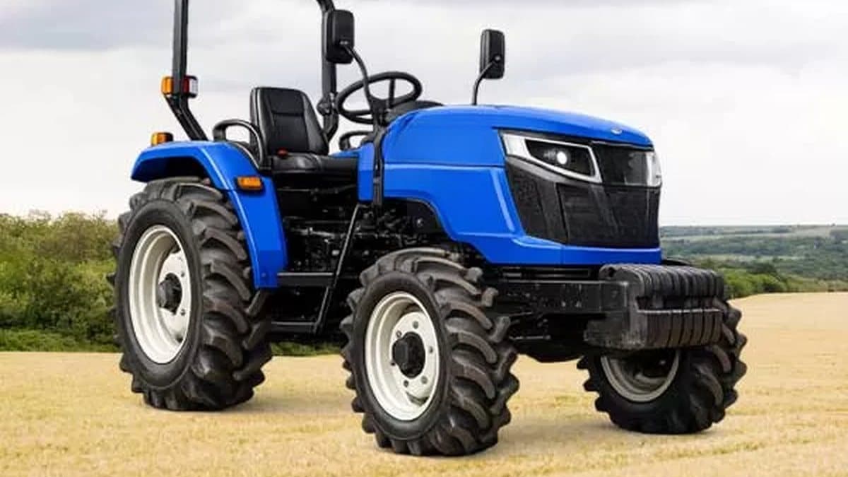 A blue battery-electric compact tractor with a roll bar, standing in a harvested field